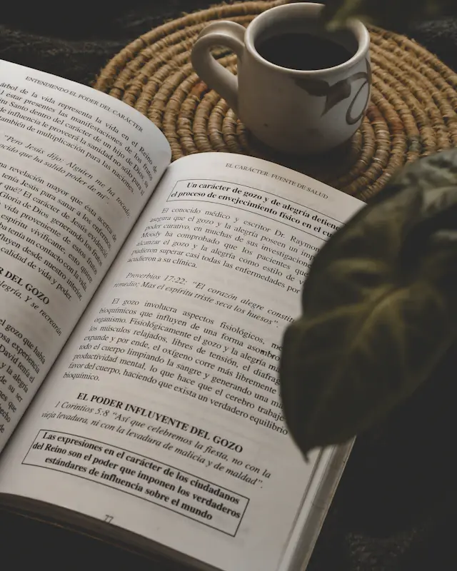 An open book and a cup of coffee beside a leafy plant.