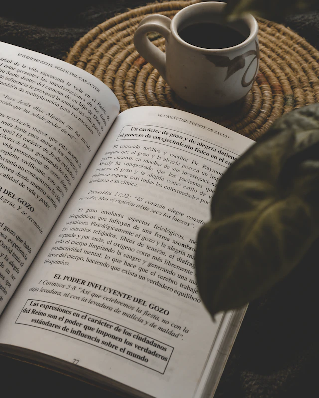 An open book with a cup of coffee and green leaves beside it.